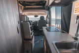 Inside a modern rv rental with a kitchenette, cozy front seats, and a serene ocean view visible through the windshield.