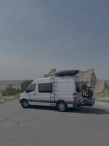 White Sprinter rv rental camper van, equipped with bikes & rooftop cargo, ready for a road trip through scenic badlands.