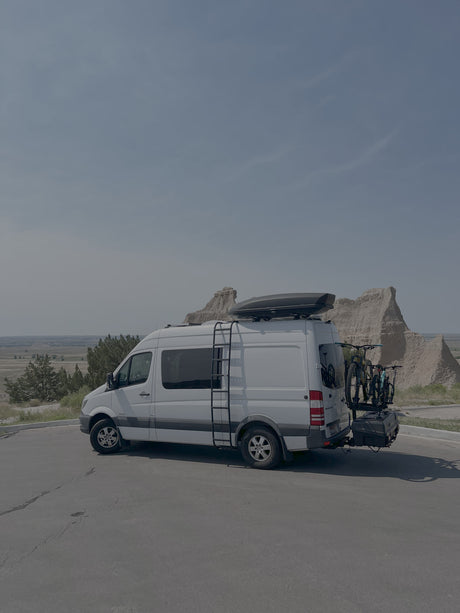 White Sprinter rv rental camper van, equipped with bikes & rooftop cargo, ready for a road trip through scenic badlands.