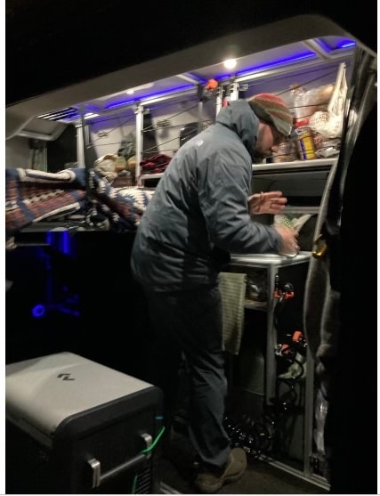 Inside an RV rental, a person with a winter hat accesses food from custom storage, illuminated by blue LEDs, showcasing mobile living. — photo 6