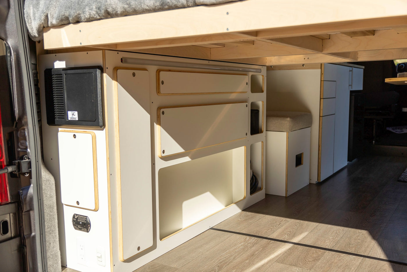 Inside this RV rental, discover the smart layout: custom camper van bed and storage, integrated electrical panel, and cushioned bench. — photo 9