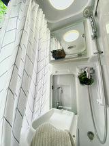 Bright RV rental bathroom featuring a shower, sink, mirror, and a white curtain with an abstract geometric pattern.