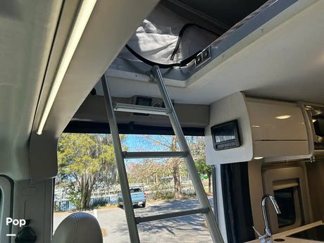 Explore this RV rental interior: a ladder accesses the pop-top sleeping area, with controls & a sink visible. Enjoy the scenic view!