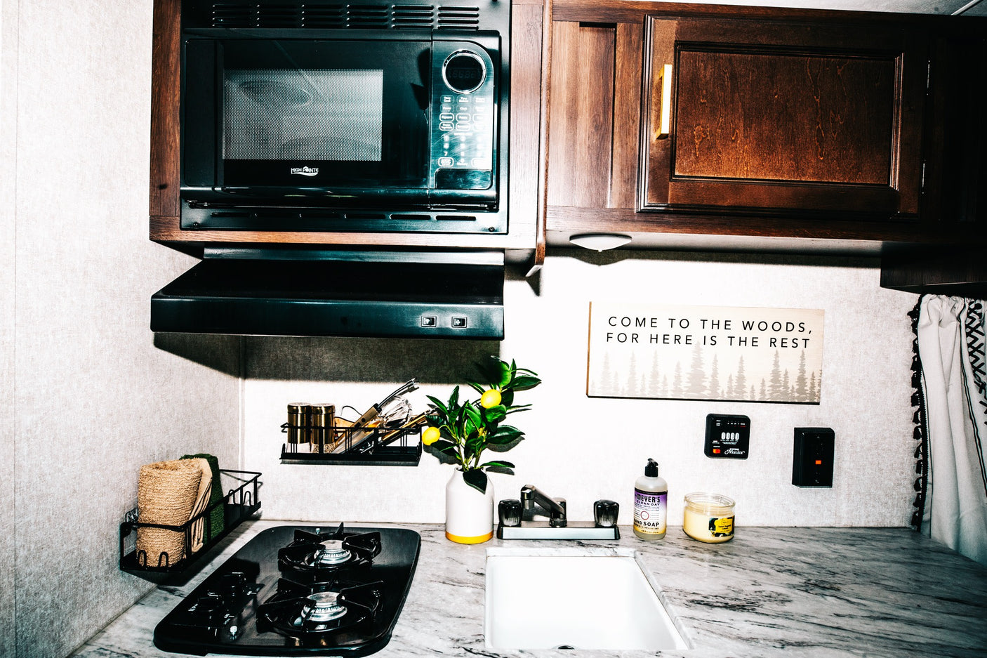 Cozy RV rental kitchen featuring a High Pointe microwave, stovetop, sink, marble-patterned counter, and "woods" sign.