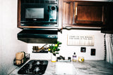 Cozy RV rental kitchen featuring a High Pointe microwave, stovetop, sink, marble-patterned counter, and "woods" sign.