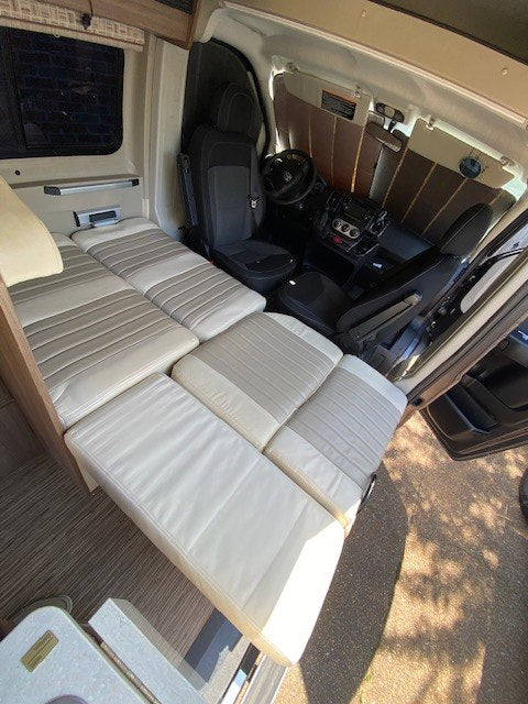Spacious RV rental interior with versatile seating that converts into a comfortable bed, extending into the front cab area.