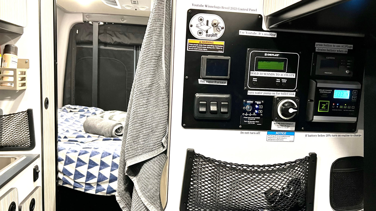 RV rental interior: A camper van's control panel, showing switches and displays for heating, water, and solar charge, beside a cozy bed.