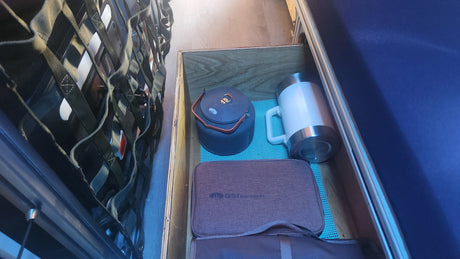 RV rental's clever storage holds a grey camping kettle, white mug, and GSI Outdoors case, on a blue mat.