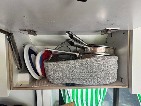 Organized kitchen essentials in an upper cabinet of an rv rental, featuring stacked pans, lids, and collapsible dishes.