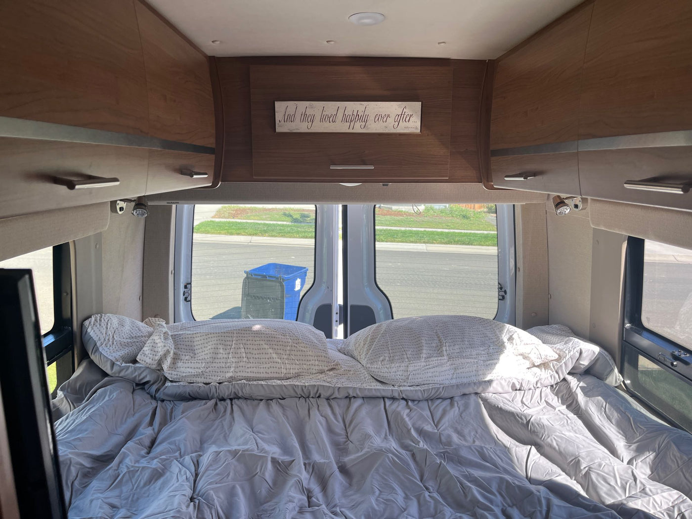 Cozy RV rental interior with a bed, overhead cabinets, and a "happily ever after" sign above. — photo 13