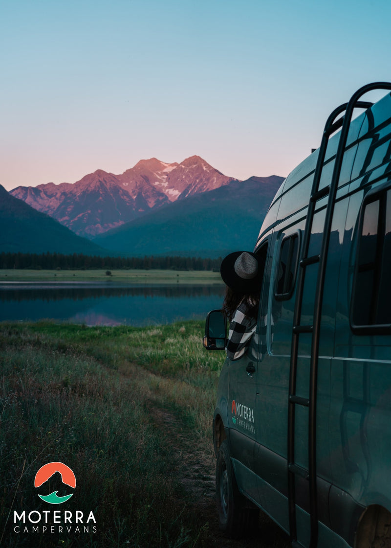  featuring a sleek shower stall on the right and a comfortable bedroom with a bed & window beyond.|View of a compact RV rental kitchen featuring a light wood countertop — photo 3