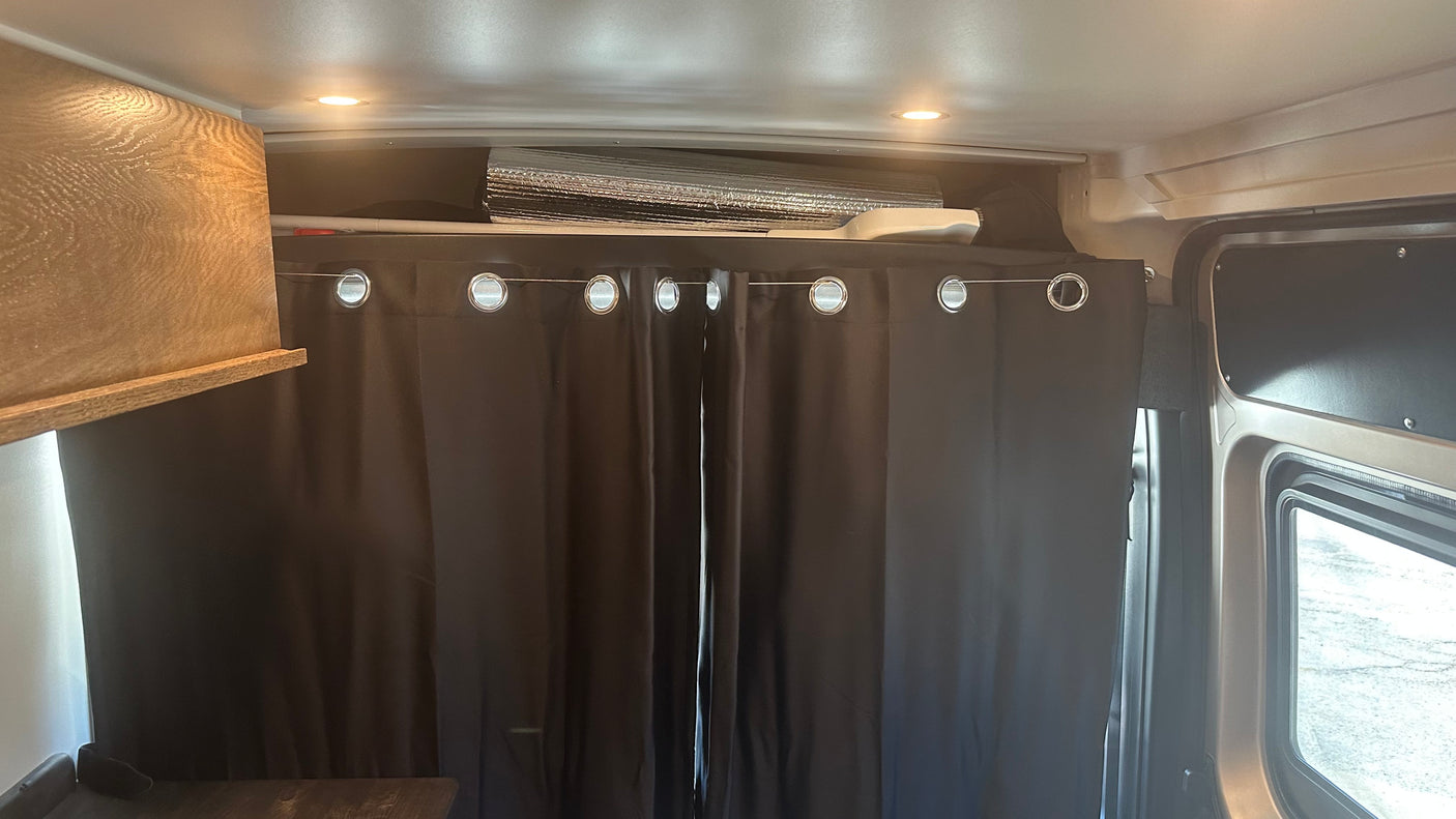 Cozy RV rental interior showing blackout curtains, overhead storage, and LED lighting for comfort.