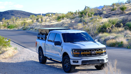 Light Ford F-150 with a bed-mounted camping system on a desert road. Perfect rv rental for off-road adventure.
