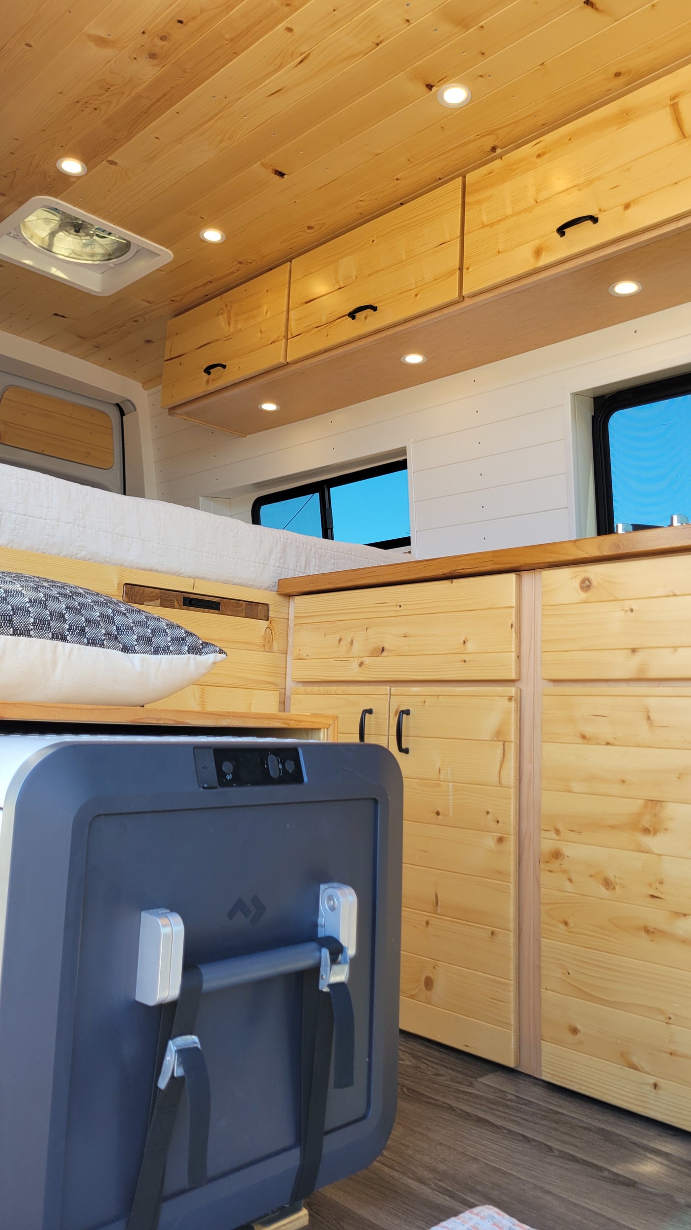 Inside a cozy rv rental with wooden ceilings, walls, and cabinetry. A bed and portable fridge complete this comfortable mobile home.