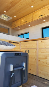 Inside a cozy rv rental with wooden ceilings, walls, and cabinetry. A bed and portable fridge complete this comfortable mobile home.