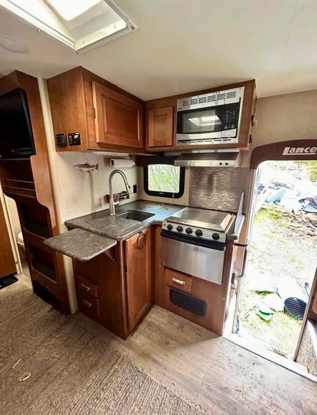 Explore this RV rental's compact kitchen with a sink, stove, microwave, and fold-out counter for efficient space use.