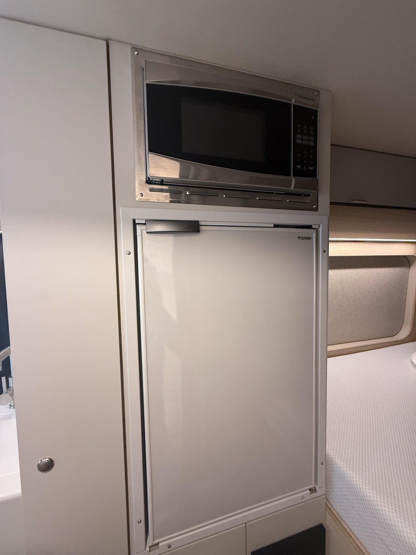 Inside an RV rental: built-in microwave and refrigerator in a compact kitchen setup, adjacent to a bed. — photo 15