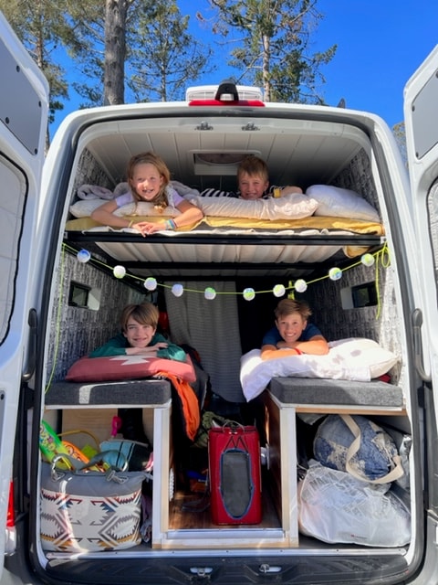 Four smiling kids peek from cozy bunks and storage cubbies inside a fun RV rental camper van, ready for family adventures. — photo 8