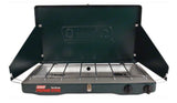 A dark green Coleman 2-burner propane camping stove, open with wind screens, perfect for RV rental and outdoor cooking.