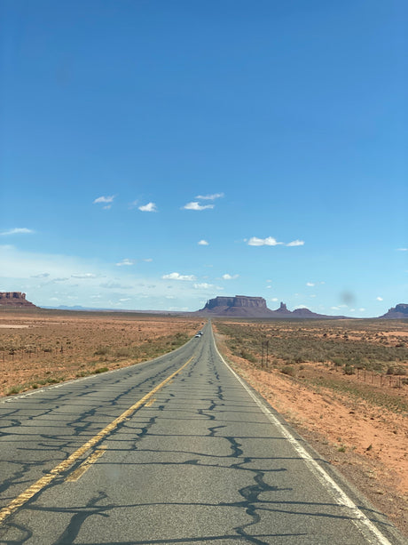 An RV rental journey through a classic desert landscape: a long highway leading to Monument Valley's majestic mesas under blue skies.