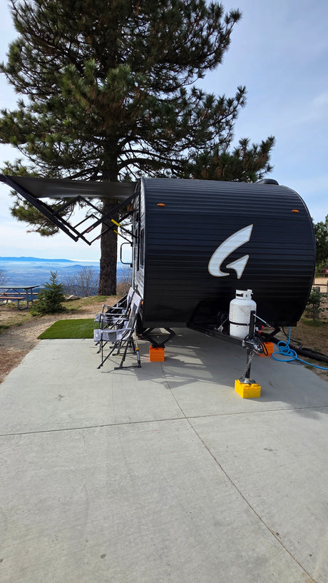 Enjoying the view from an RV rental: a black travel trailer with an extended awning parked at a scenic mountain campsite.
