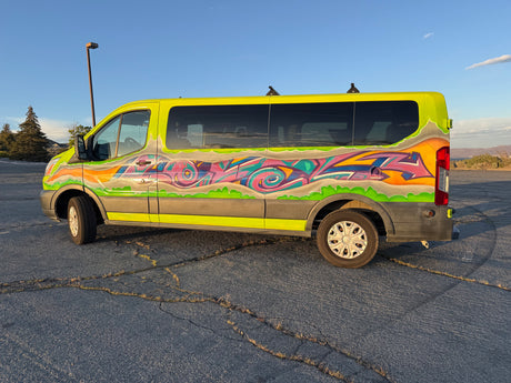Vibrant lime-green graffiti RV rental van, ready for adventure, parked on cracked asphalt under a clear blue sky.