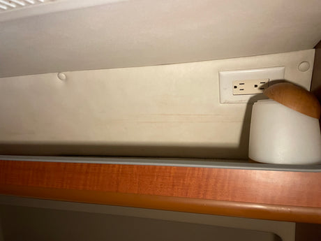 RV rental interior showing a beige wall with an electrical outlet, a cup with a wooden lid, and a wooden trim below.