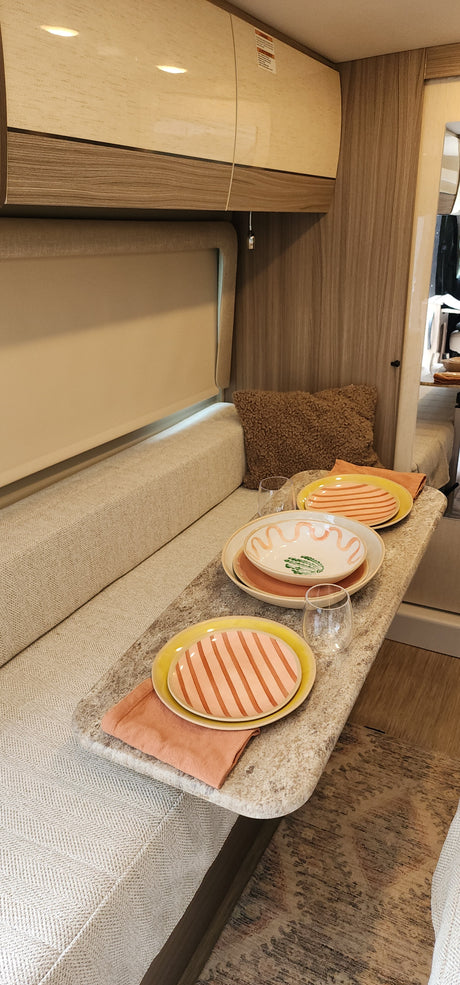 Stylish RV rental dining nook featuring comfortable bench seating and a set table with vibrant dishware.