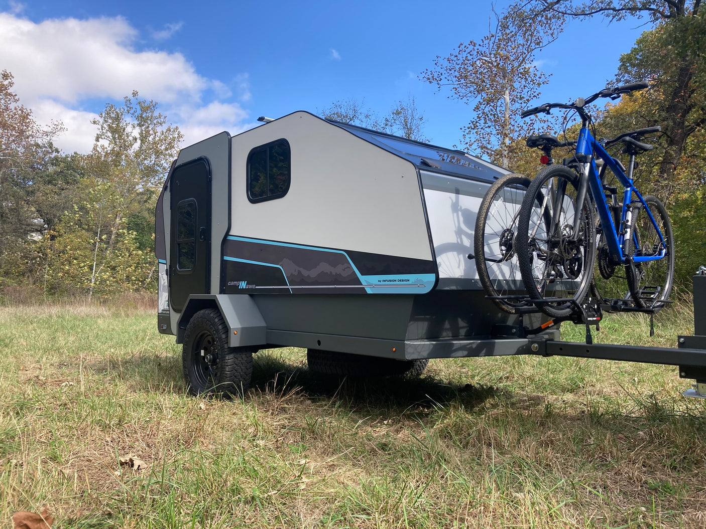 Sleek RV rental camper with two bikes mounted, parked in a sunny, grassy field under a blue sky, perfect for outdoor escapes.