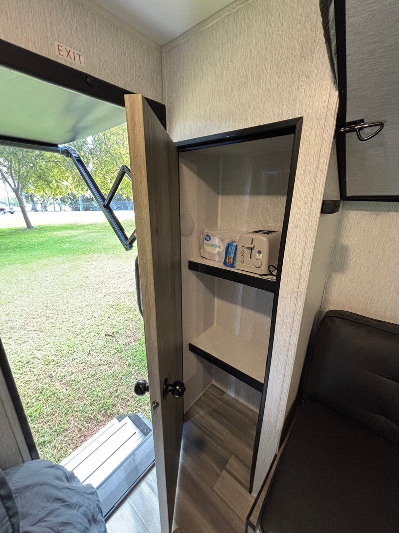 Inside an RV rental: open door reveals lush outdoors. A cabinet holds a toaster & napkins next to a black sofa. — photo 11