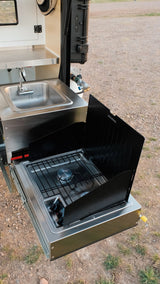 RV rental outdoor kitchen features a pull-out stainless steel sink and gas stove with wind guards for campsite cooking.