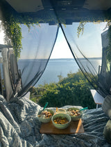 Serene RV rental escape: Breakfast bowls on a cozy bed with a stunning lake view through a bug screen.