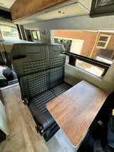 Comfortable RV rental interior: black quilted seats, wood table, and light-colored walls.