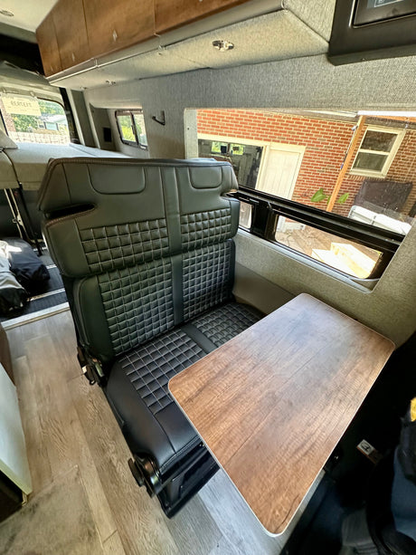 Comfortable RV rental interior: black quilted seats, wood table, and light-colored walls.