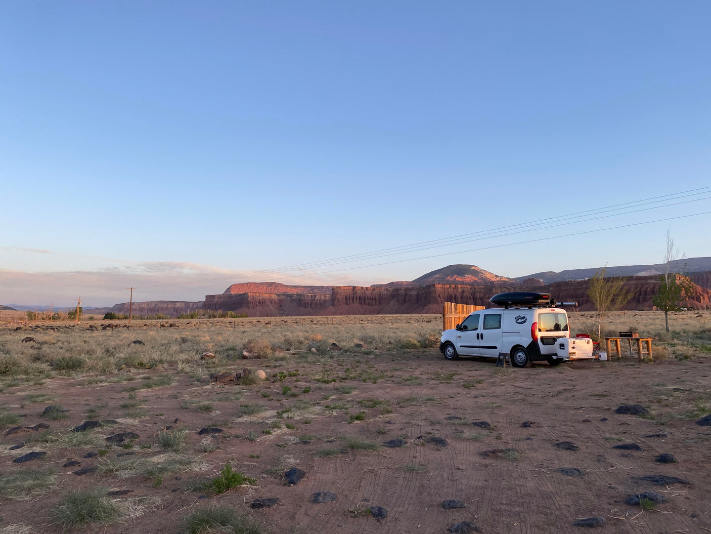 Scenic desert rv rental camping: a white camper van at sunrise/sunset, parked near stunning red rock cliffs.
