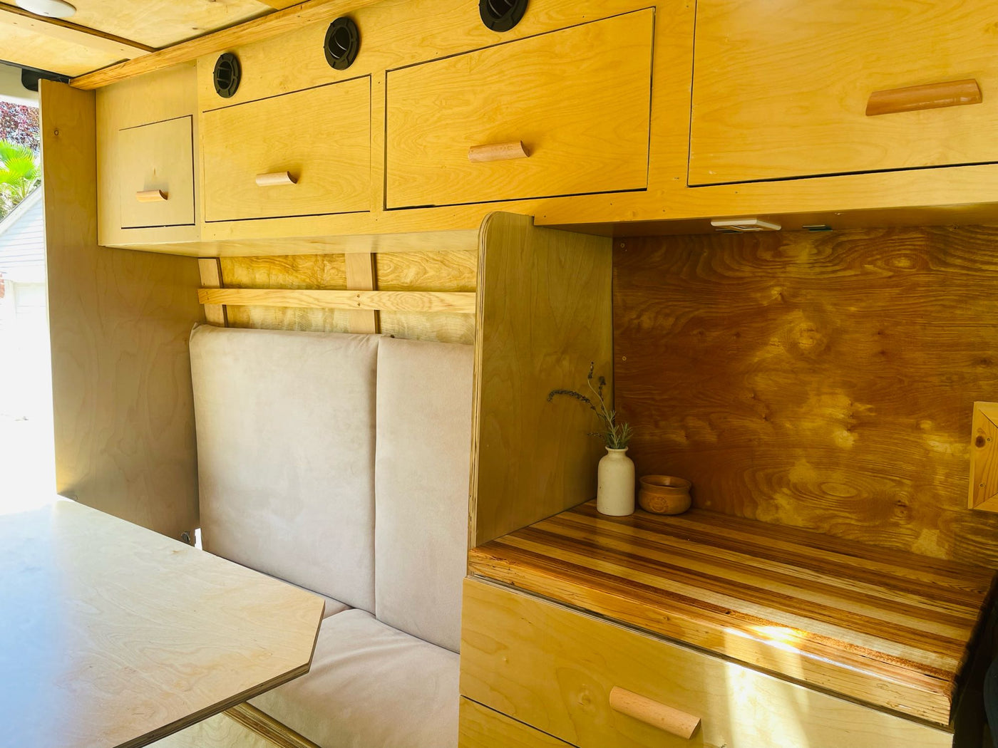Inside this light wood RV rental: custom cabinetry, comfortable bench seating, dining table & a wood-striped counter. — photo 11