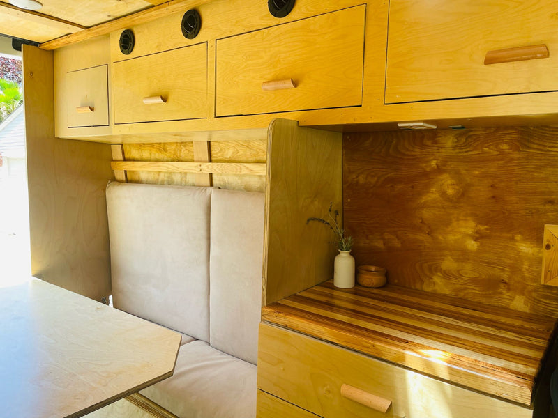 Inside this light wood RV rental: custom cabinetry, comfortable bench seating, dining table & a wood-striped counter. — photo 11