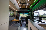 Spacious rv rental camper van interior. Features a laptop workstation, kitchen, and wood-paneled ceiling with ambient lights.