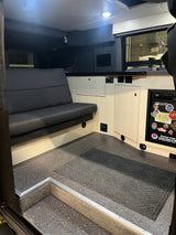 RV rental interior features a dark bench seat, light wood cabinets, and a compact kitchen area with fridge.