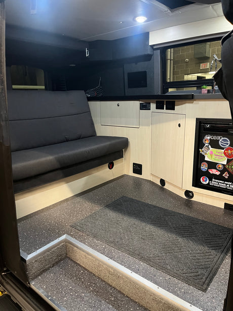 RV rental interior features a dark bench seat, light wood cabinets, and a compact kitchen area with fridge.