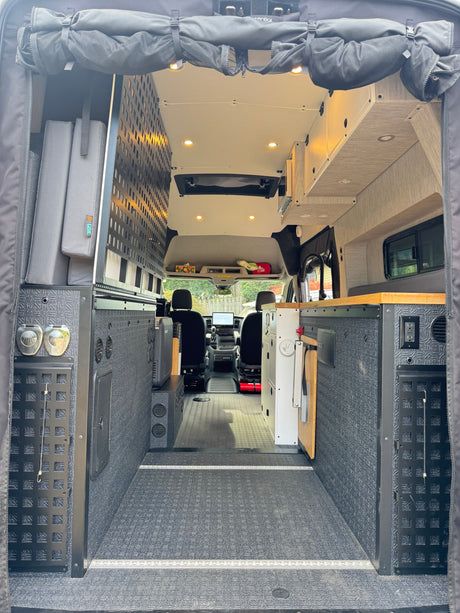 Inside a custom RV rental camper van: modular storage, a functional kitchen, & versatile living space from rear doors.