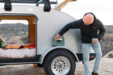 RV rental camping: Man uses a portable power station outside his teardrop camper for off-grid power.