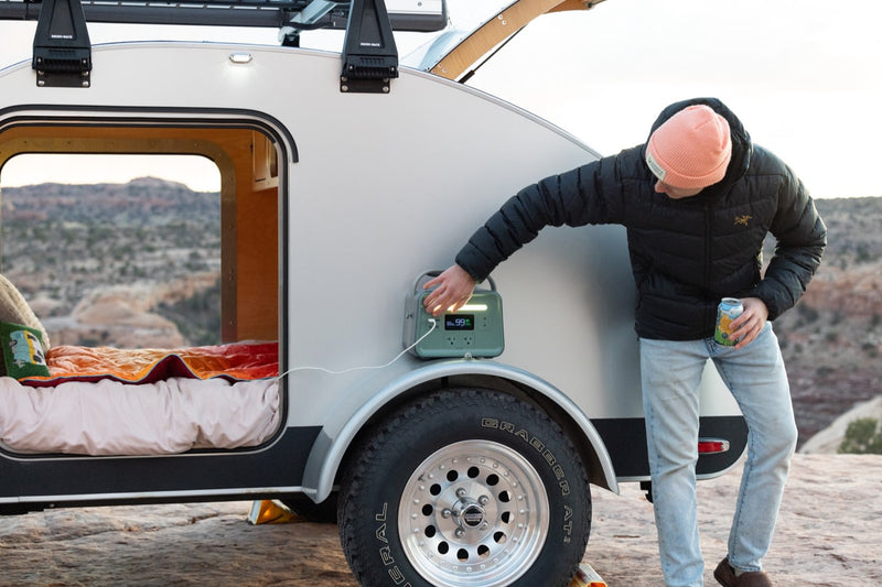  powered for off-grid adventures.|RV rental camping: Man uses a portable power station outside his teardrop camper for off-grid power.|Cozy rv rental bed with wood interior — photo 10