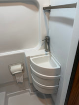 An RV rental compact wet bath. White interior with corner sink, modern faucet, and toilet paper holder, ideal for small spaces.