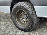 Off-road tire and custom wheel on an adventure-ready RV rental, parked on a gravel surface.