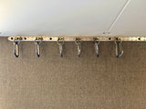 RV rental storage: Six metal carabiner hangers on a track, useful for organizing items in a compact space.