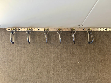 RV rental storage: Six metal carabiner hangers on a track, useful for organizing items in a compact space.