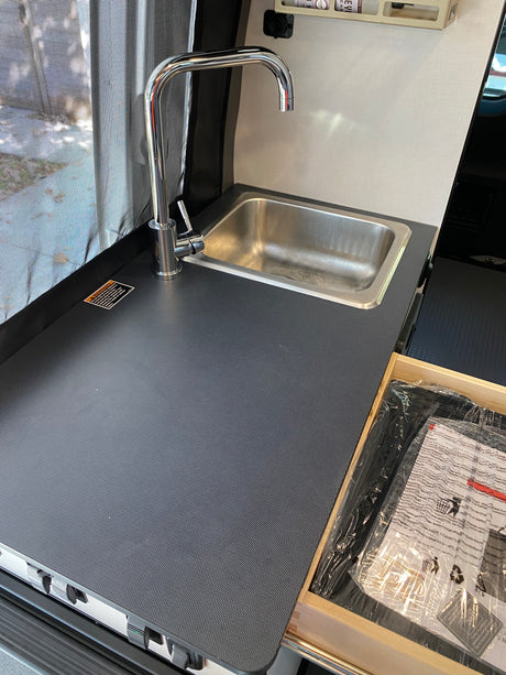 Inside an RV rental: a compact kitchen area with a stainless steel sink, chrome faucet, and textured gray countertop.