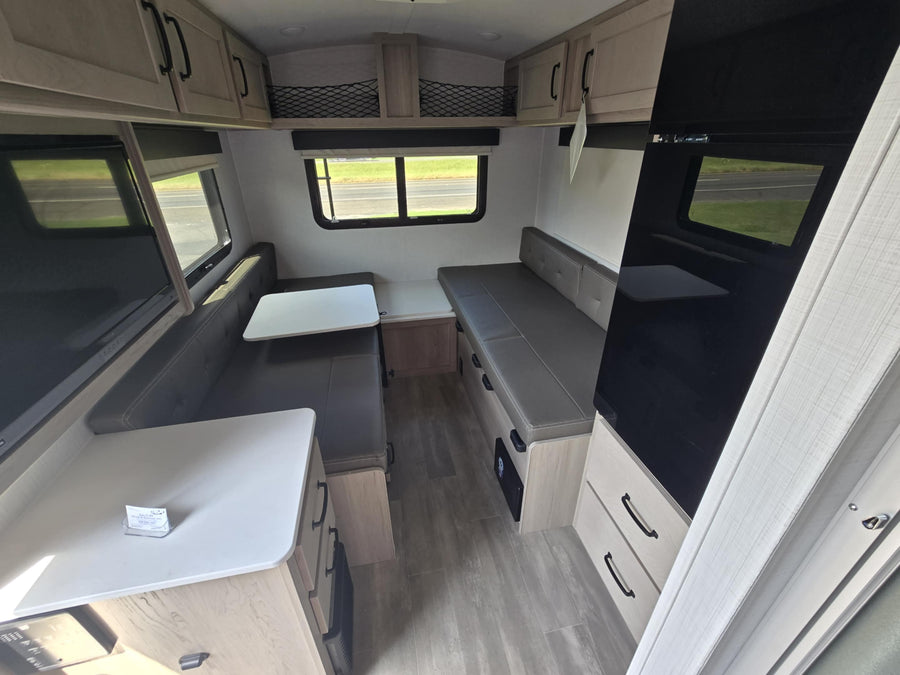 Compact RV rental interior featuring a convertible dinette, sleek cabinets, and ample seating.