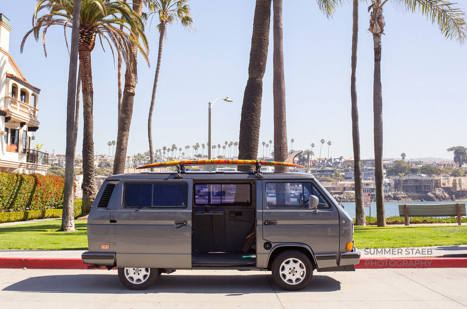 Vintage VW Vanagon RV rental with a surfboard, ideal for coastal adventures & beach life.